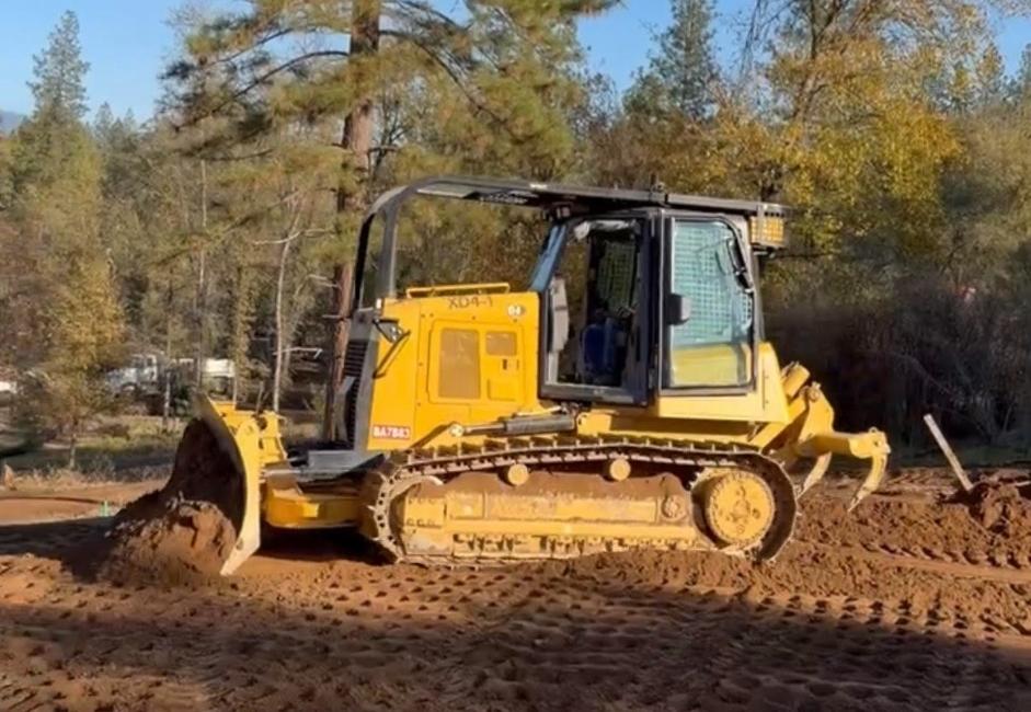 Yellow crawler dozer performing house pad grading work on foothill soil
