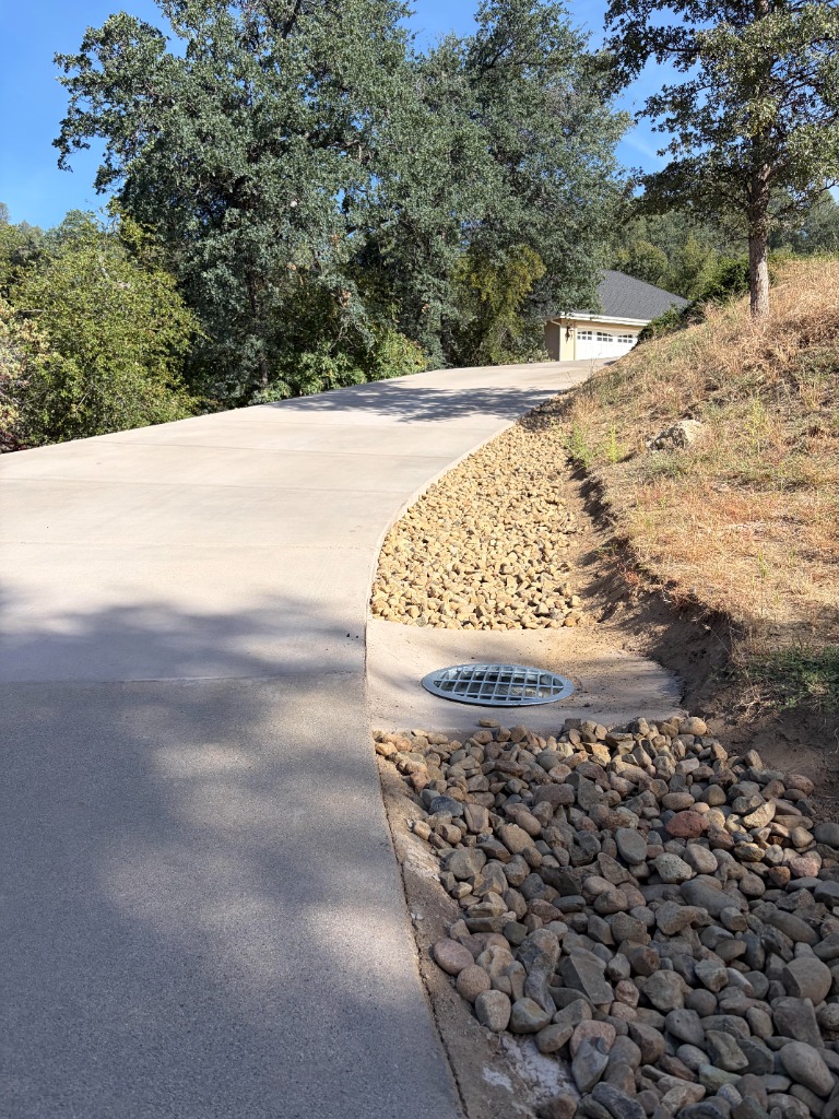 Finished concrete driveway winding up to a house with gravel drainage on the side