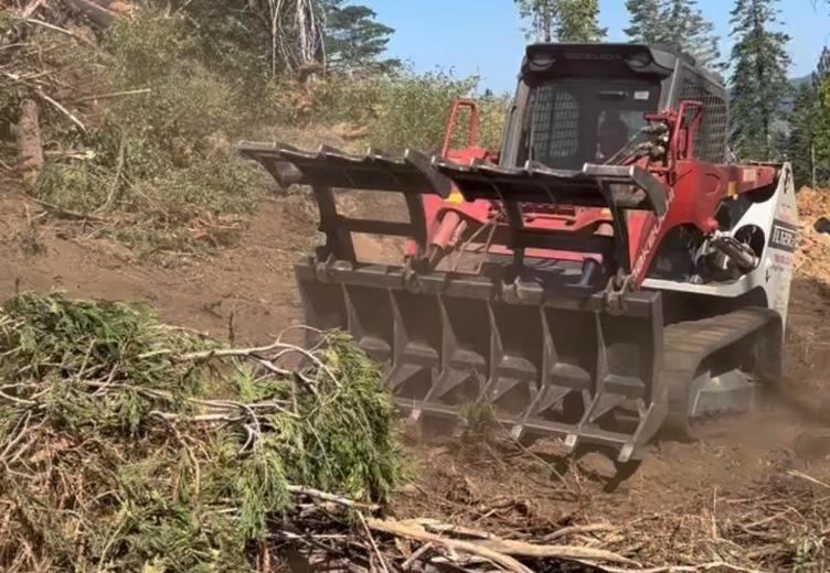 Takeuchi track loader with grapple attachment clearing brush and logs on a hillside
