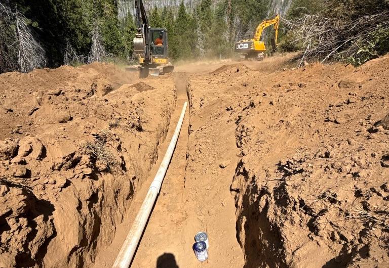 White water pipeline laid in a dirt trench with excavators on site